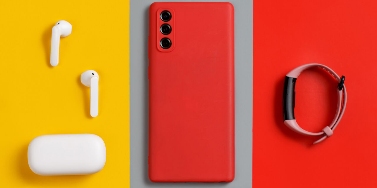 Smartphone, white wireless earphones awith the case and  smart watch top view on red, grey and yellow background