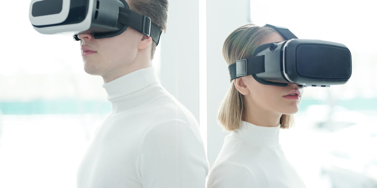 Young people in white sweaters wearing virtual reality goggles standing back to back